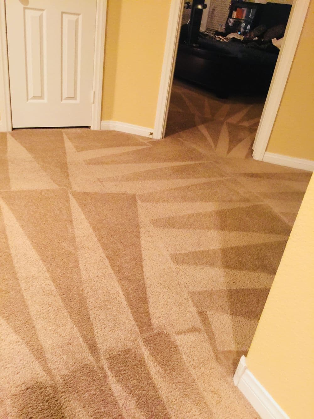 Diagonal patterns on beige carpet flooring in a well-lit hallway with yellow walls.