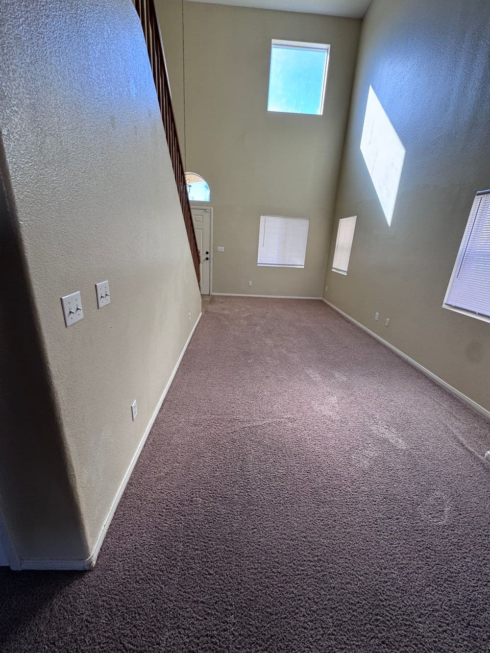 Spacious living room with carpet, tall ceilings, and large windows for natural light.