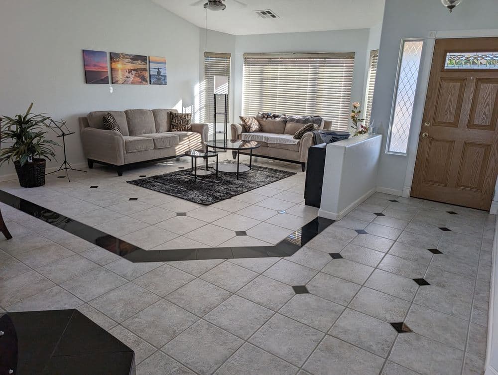 Bright living room with beige sofas, tiled flooring, and large windows, showcasing a cozy interior.
