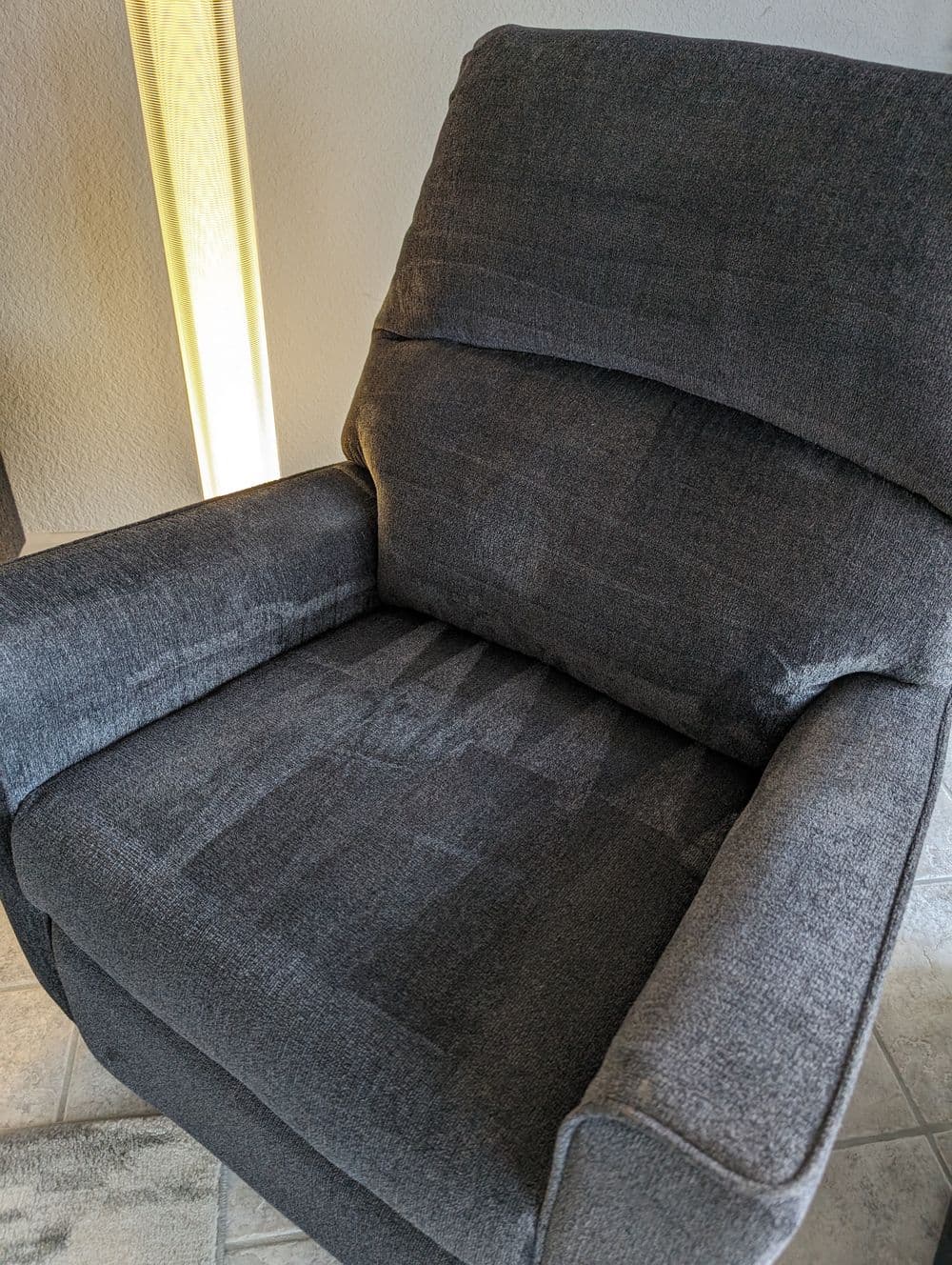Gray upholstered reclining chair with plush cushions and a modern design in a cozy interior.