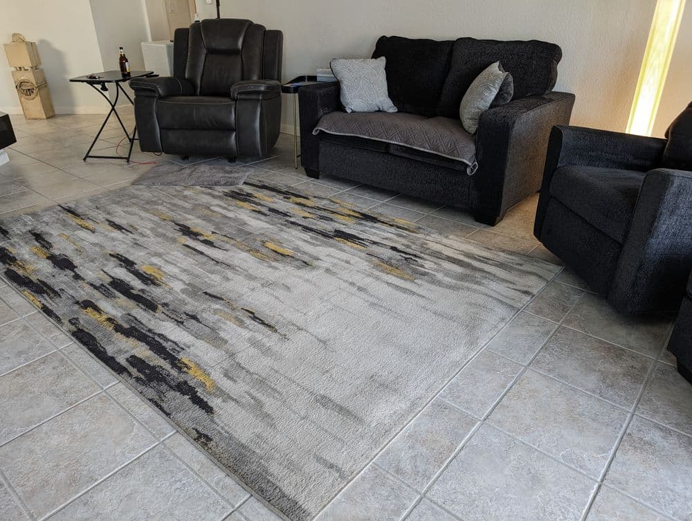 Modern living room with textured area rug, black sofa, reclining chair, and tiled floor.