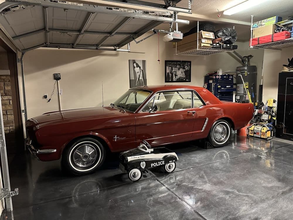 Classic 1964 red Mustang parked in a garage with a toy police car nearby.
